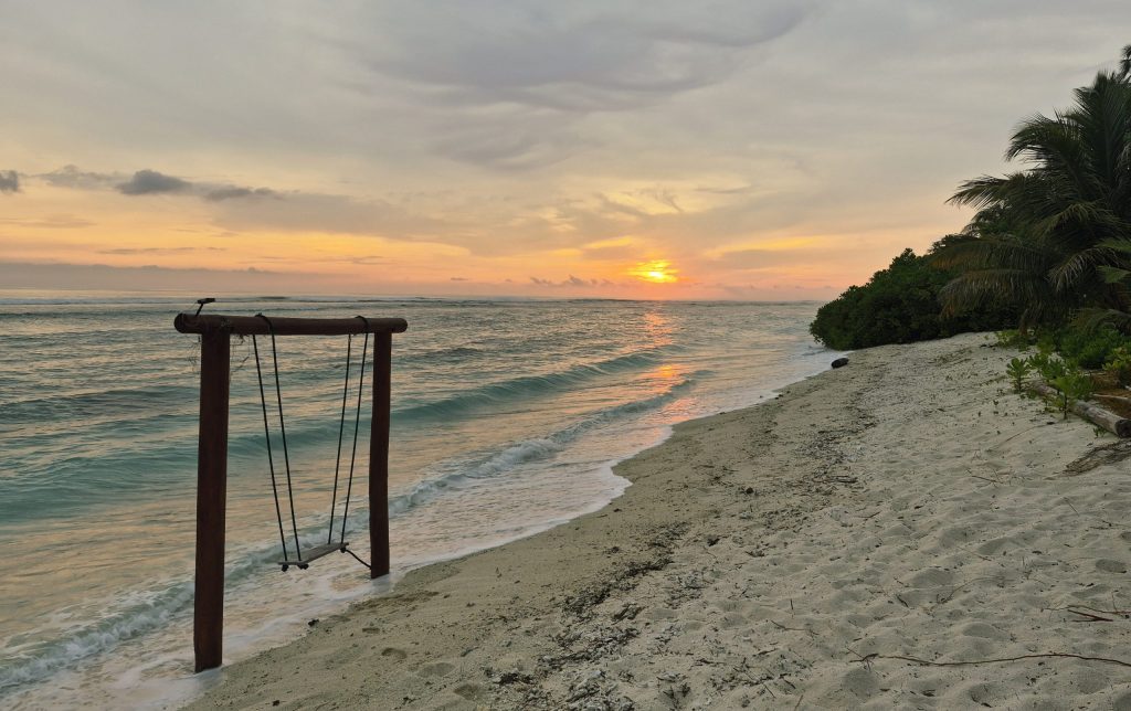 Plage tropicale au coucher du soleil avec une balançoire en bois face à la mer